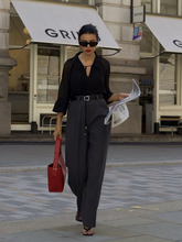 a lady wears a black silk blouse and black pants with a red handbag